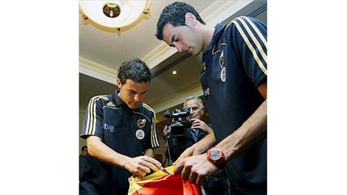 Juan Mata y Sergio Busquets firman una bandera española tras la rueda de prensa que ofrecieron hoy e