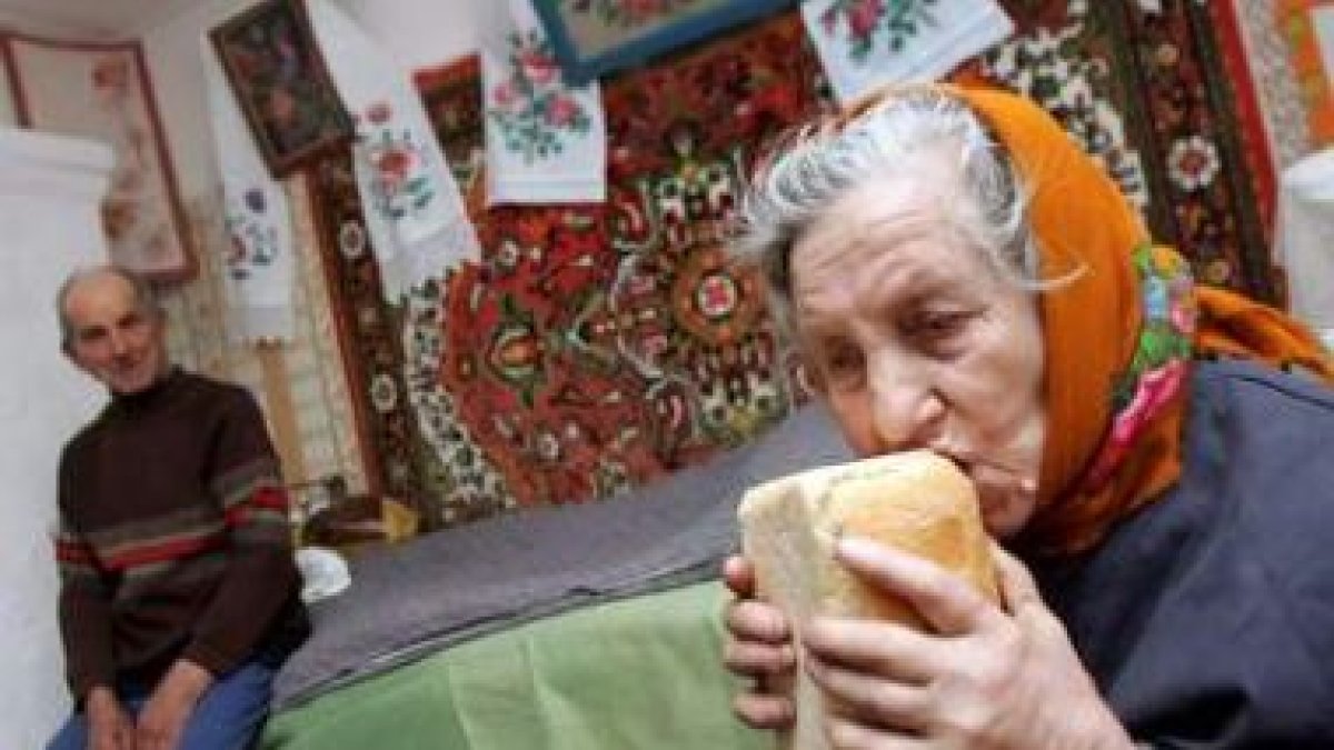 Una anciana prueba un pan ante la presencia de su marido en su casa de Ucrania.