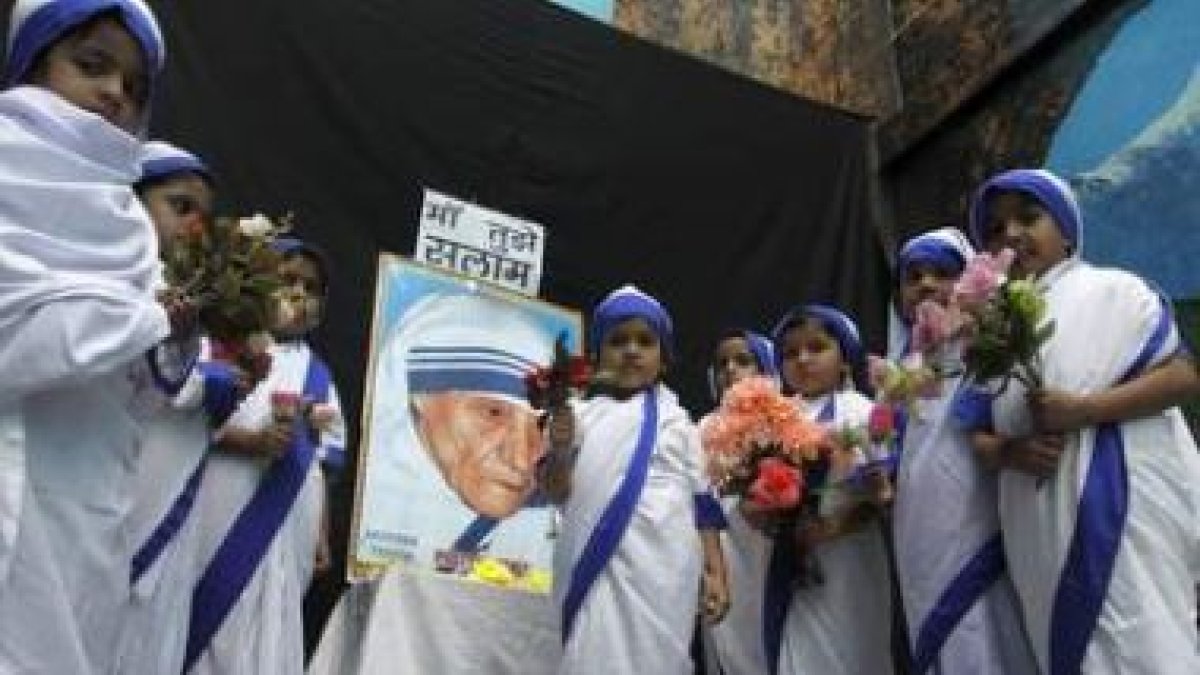 Niñas vestidas como Misioneras de la Caridad realizan una ofrenda floral frente al retrato de la Mad
