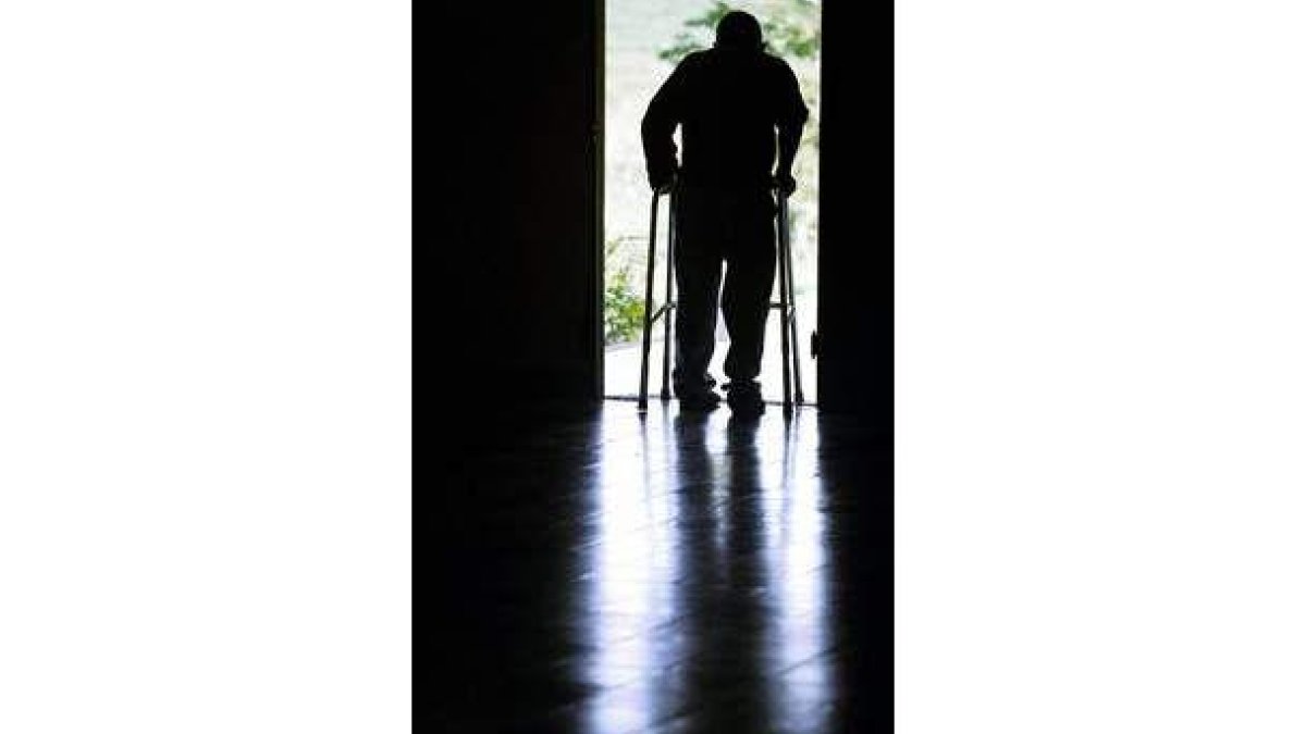 Un anciano camina con ayuda en una residencia.