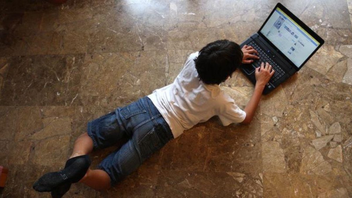 Un niño navega por internet tumbado en el suelo de su casa.