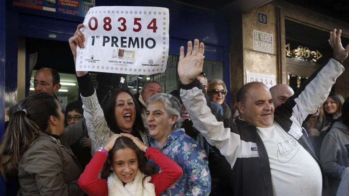 Agraciados con el primer premio del sorteo de El Niño, dotado con 2.000.000 de euros a la serie, lo celebran con el número en la mano, en las puertas de la administración número 3 de Torrent.