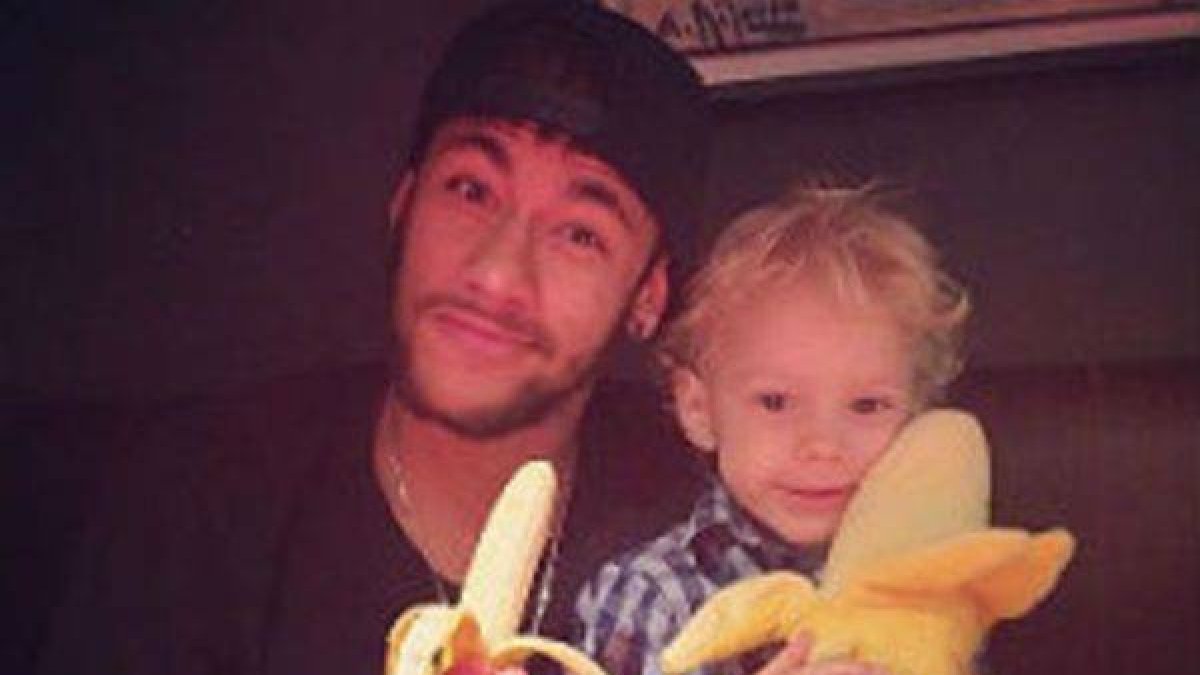 Neymar se come un plátano junto a su hijo, que sostiene un plátano de peluche.