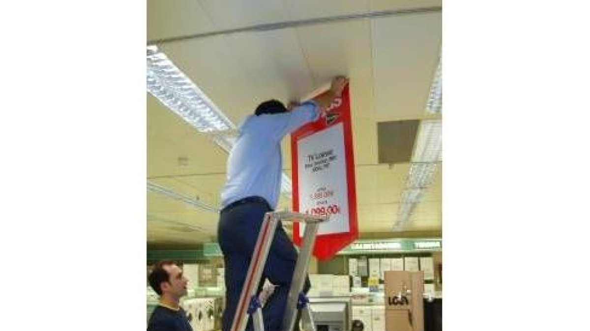 Uno de los trabajadores cuelga un cartel anunciador de las rebajas