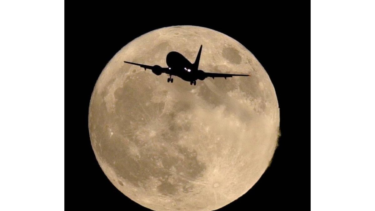 La silueta de un avión se perfila a su paso frente a la luna llena
