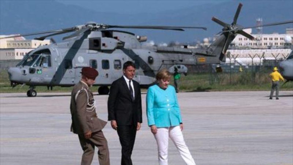 Renzi, Merkel y un oficial tratan de ajustar la alfombra roja en el aeropuerto de Nápoles, antes de desplazarse a Ventotene.