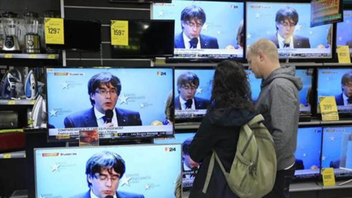 Una pareja sigue la rueda de prensa de Puigdemont en una tienda del Poblenou.