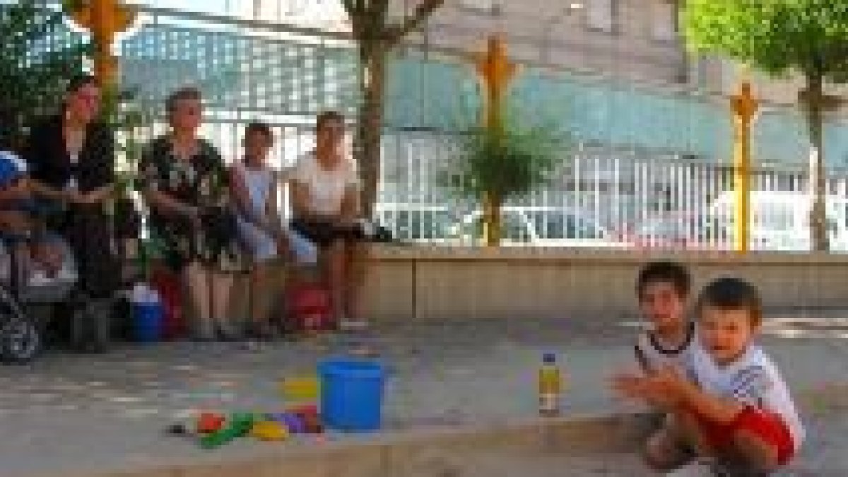 Dos niños juegan con la arena del parque infantil ante la mirada de sus familiares