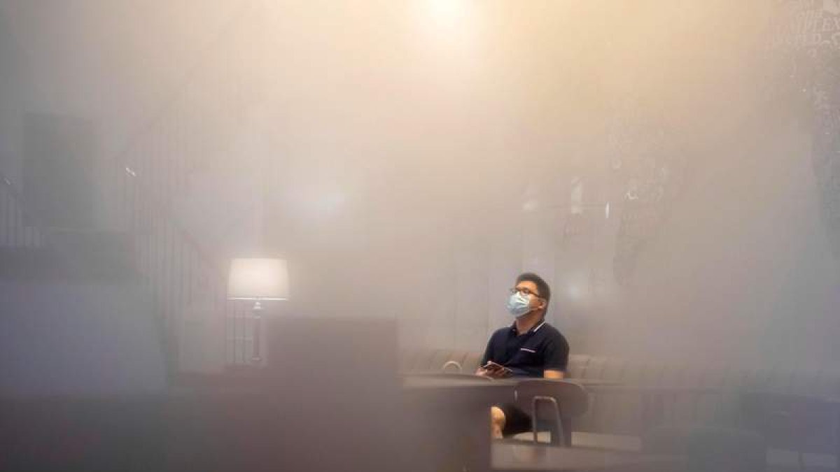 Un hombre con mascarilla sentado en un café con los cristales empañados