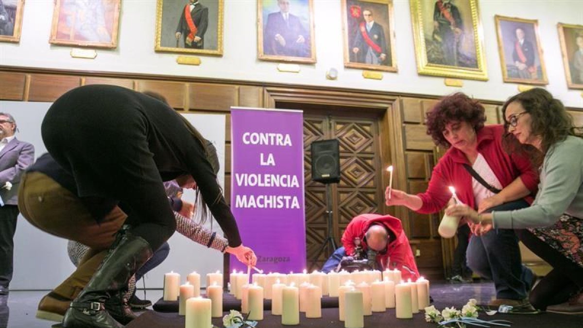 Asistentes al acto de homenaje a las víctimas de la violencia machista que se ha celebrado hoy en el consistorio zaragozano, encienden unas velas.