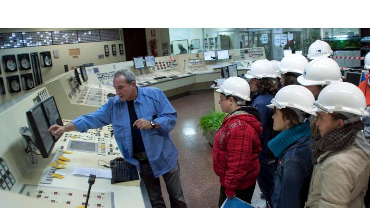 Un operario de la eléctrica muestra un cuadro de control a un grupo de jóvenes estudiantes.
