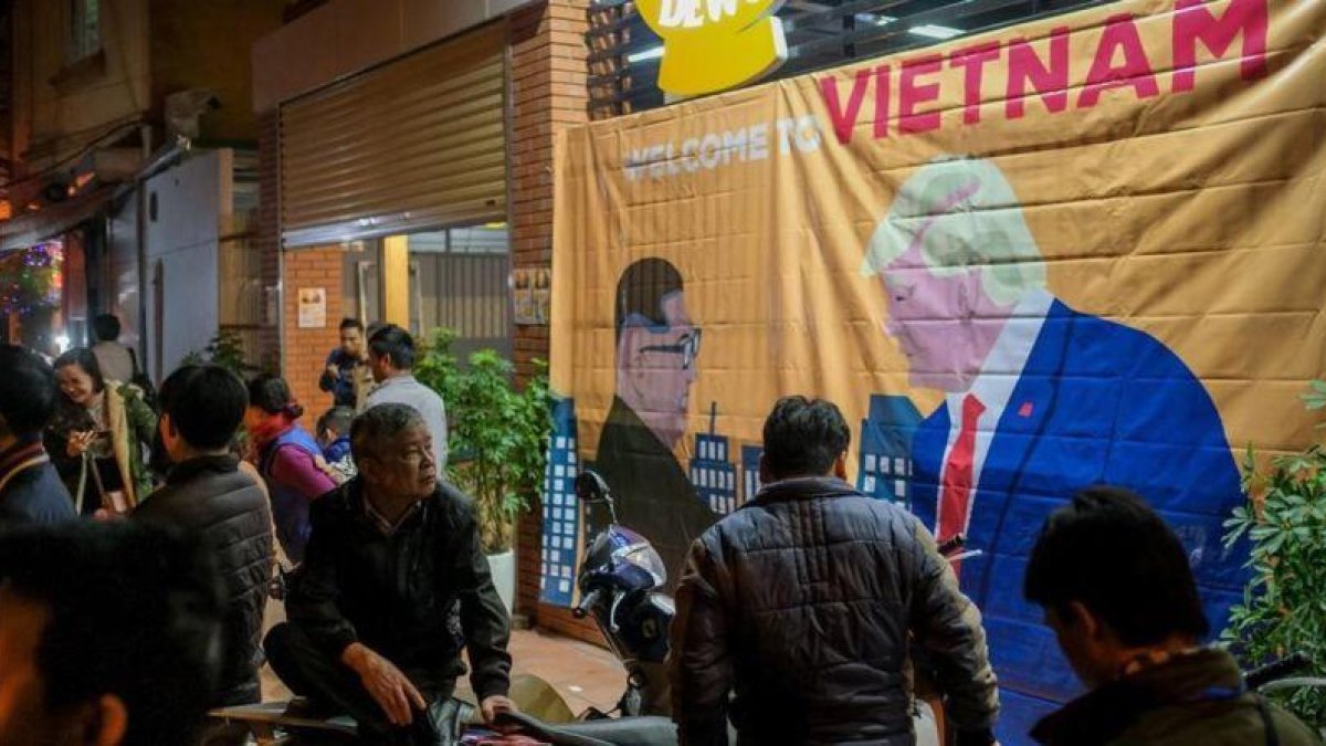 Ciudadanos de Hanói pasan ante un cartel con las imágenes de Kim y Trump horas antes de su encuentro.