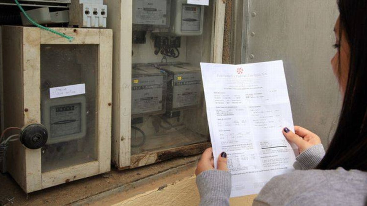 Una mujer revisa la factura de la luz junto a un contador.