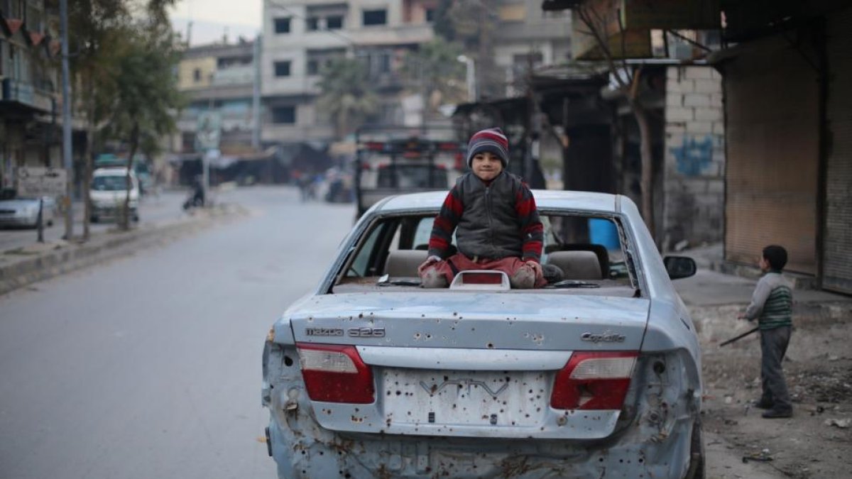Un niño sirio sentado sobre un coche dañado por las explosiones del este de Ghouta.