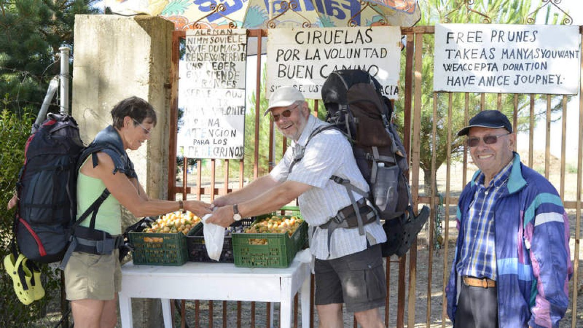 Dos peregrinos aprovechan la oferta de Carlos Rivero (derecha), que ofrece su mercancía a las puerta de su finca.