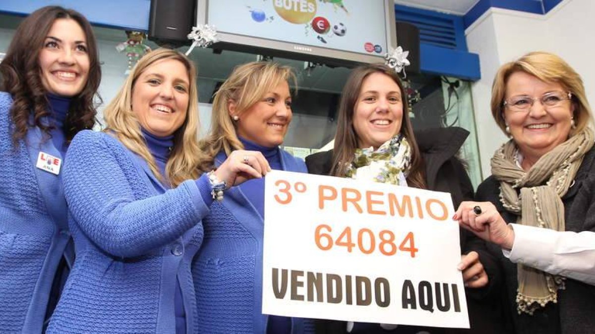 La lotera Ana María González (derecha) sujeta el cartel de premio con sus hijas y la agraciada Beatriz Pérez, a su lado.