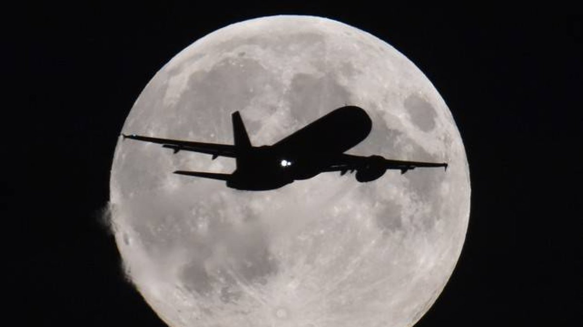 Un avión se acerca al aeropuerto de Heathrow (Londres) con la luna llena al fondo.
