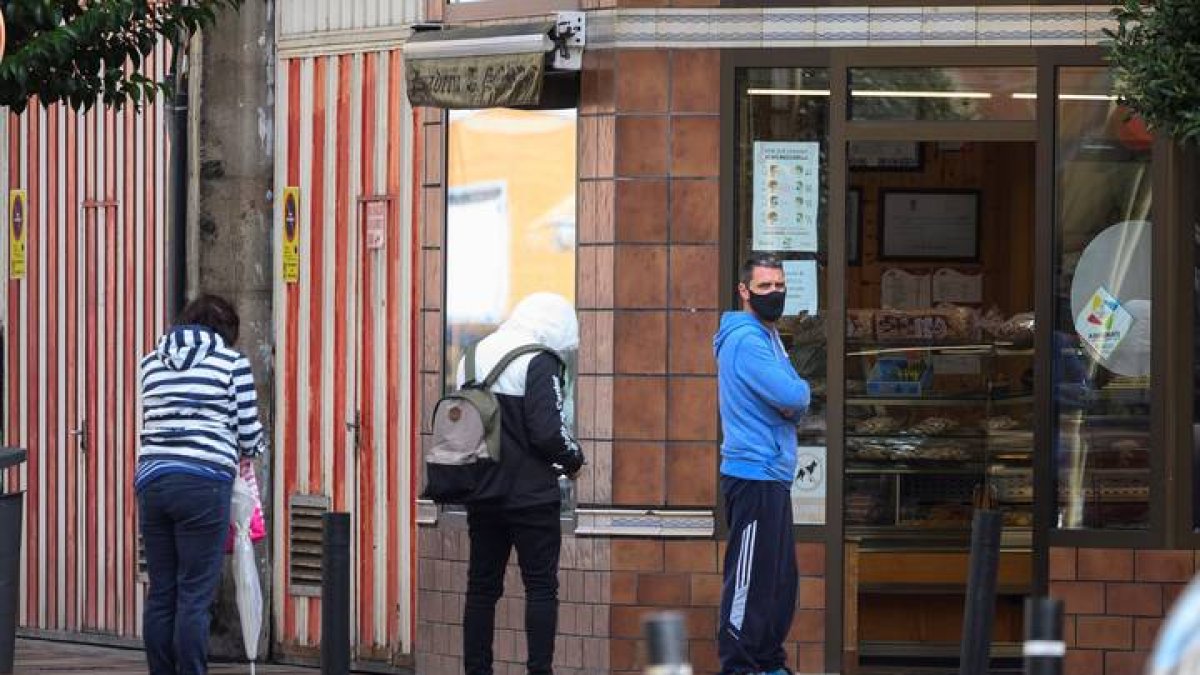 Varias personas esperan en la entrada de un comercio en el barrio de La Inmobiliaria en Torrelavega. PEDRO PUENTE HOYOS