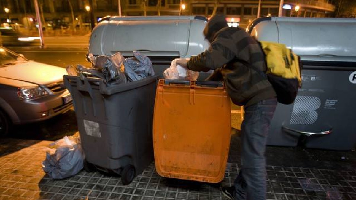 Un joven busca comida en un contenedor de basura orgánica, en Barcelona.