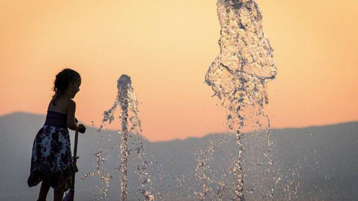 Una niña se refresca en una fuente.