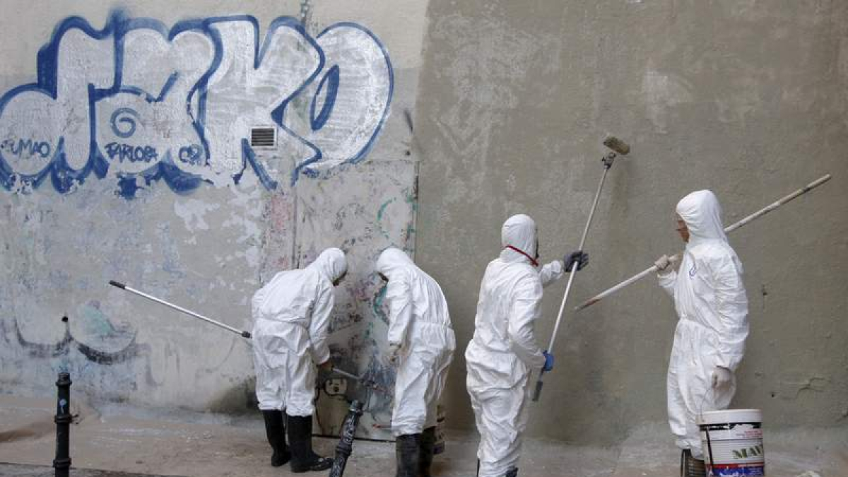 Grafiteros limpian las pintadas para saldar la multa que les ha puesto el Ayuntamiento.