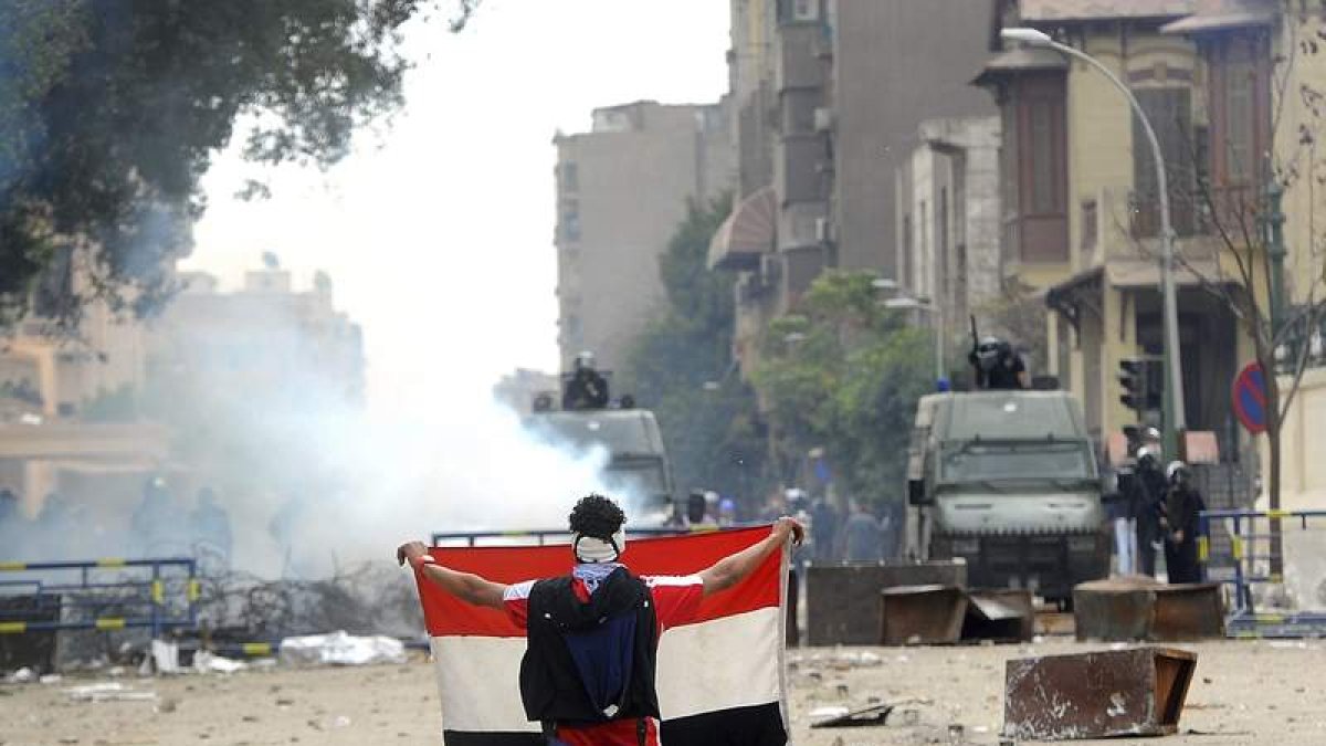 Un manifestante muestra una bandera egipcia a la policía, detrás de la barricada.
