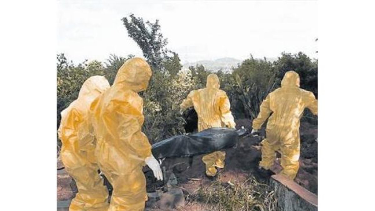 Personal sanitario con trajes de aislamiento traslada el cuerpo de una posible víctima de ébola en Sierra Leona.