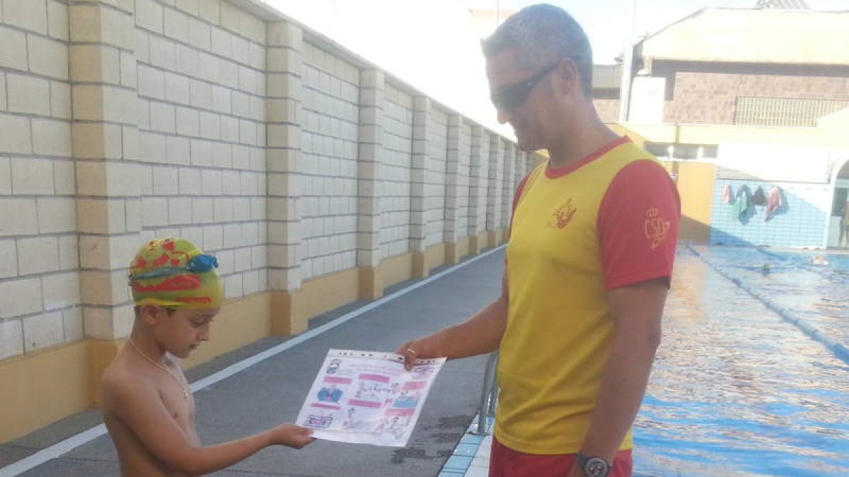 Un niño recibe el díptico donde se recogen las normas básicas para el medio acuático.