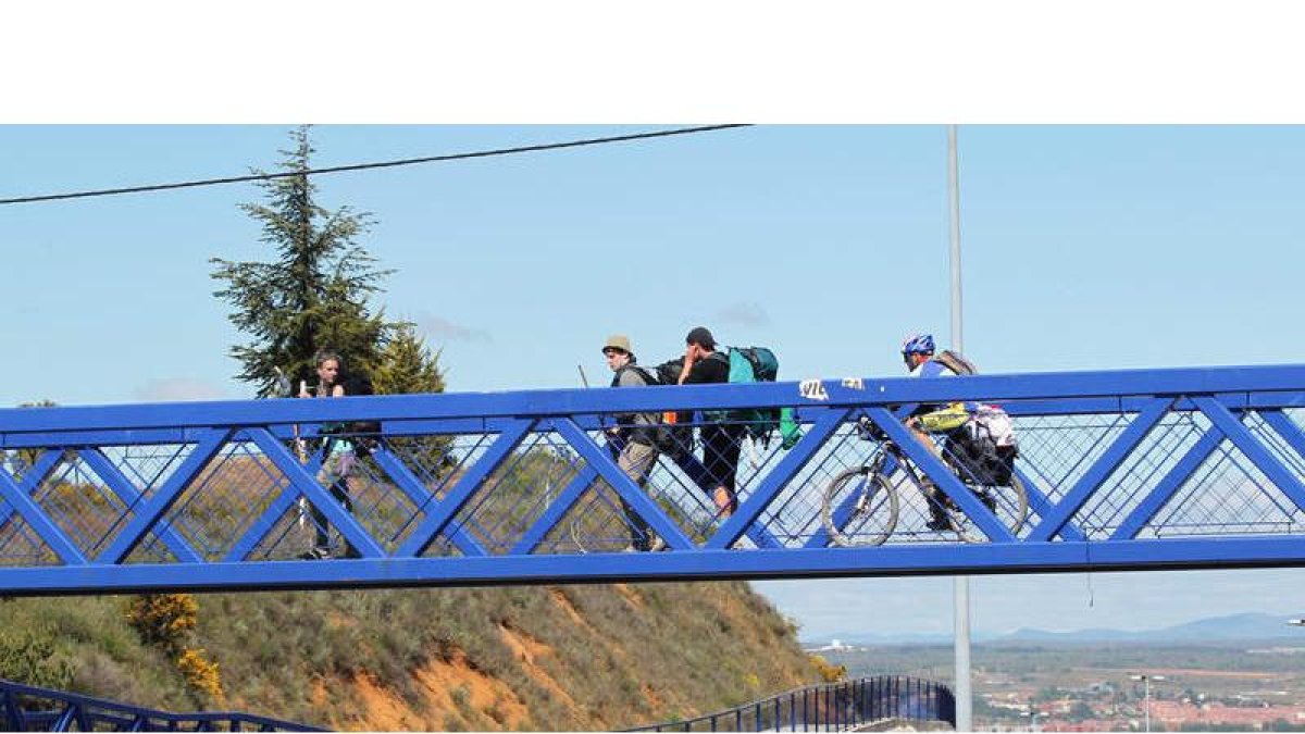 Peregrinos caminan por la pasarela del Alto del Portillo en su senda de entrada a la capital de la provincia.
