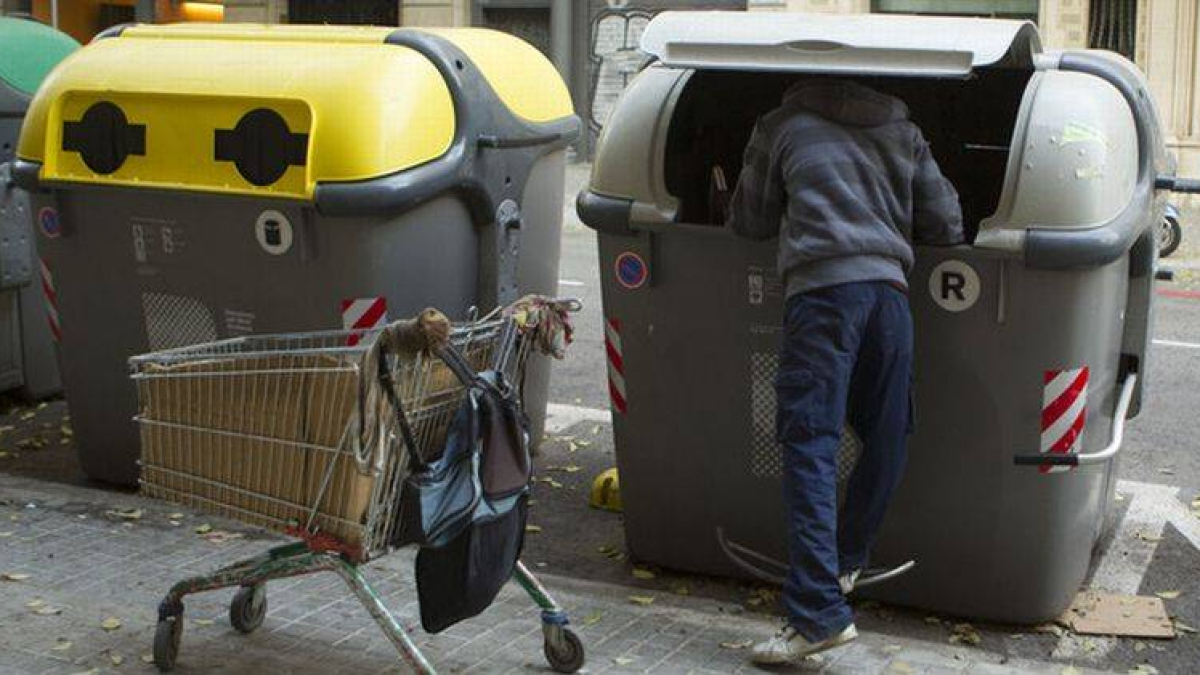 Un hombre mira dentro de un contenedor en la calle.