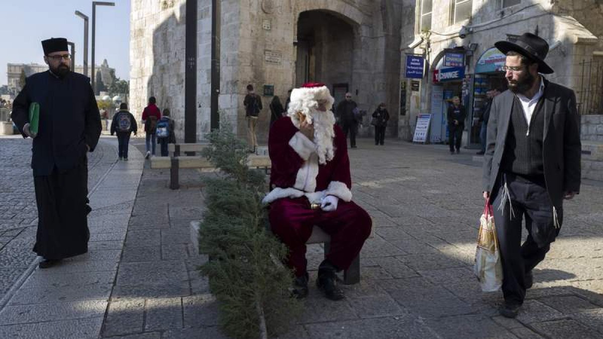 Un judíos ultraortodoxo observa con descontento a un palestino disfrazado de Papá Noel que reparte árboles.