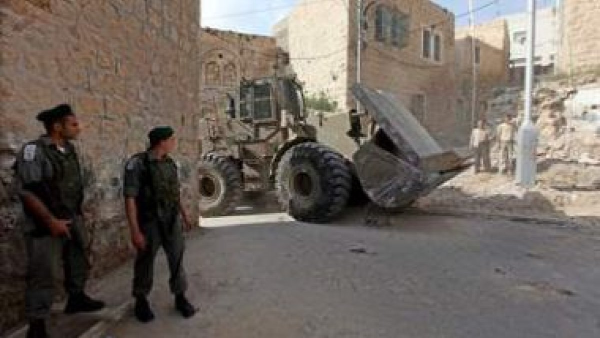 Soldados israelíes hacen guardia mientras una retroexcavadora mueve un bloque de piedra en la ciudad
