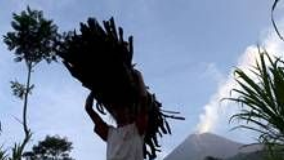Una residente porta leña mientras el monte Merapi escupe humo y lava