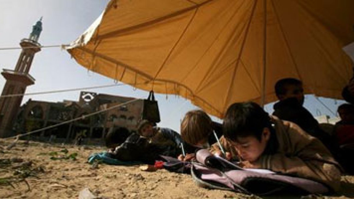 Niños palestinos asisten a clase en una tienda instalada entre los restos de su escuela destruída.