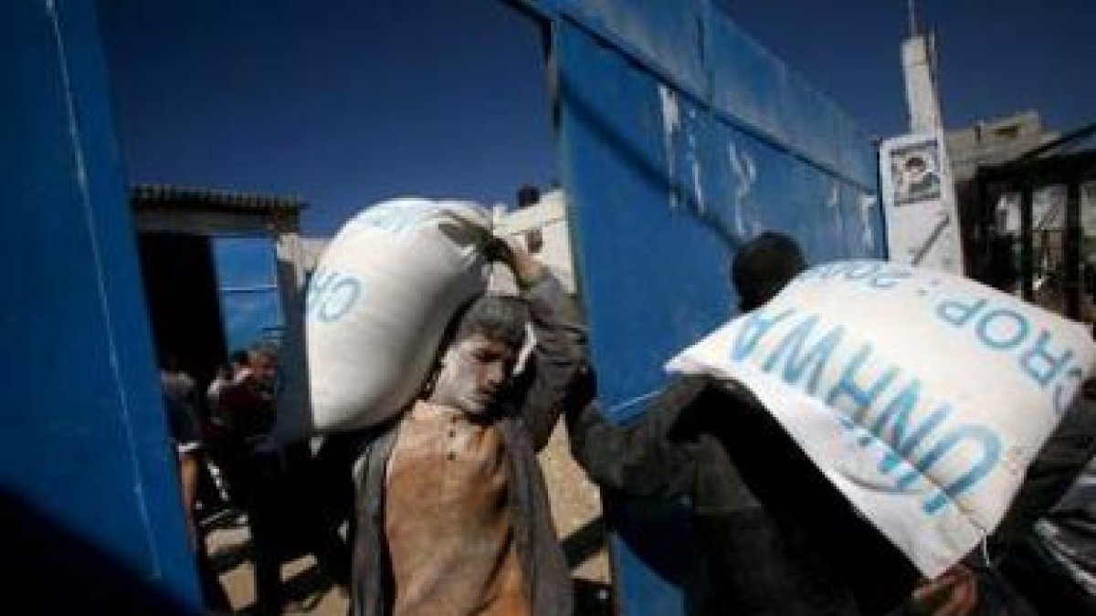 Varios palestinos cargan sacos de comida en un centro de reparto de ayuda humanitaria de Naciones Un