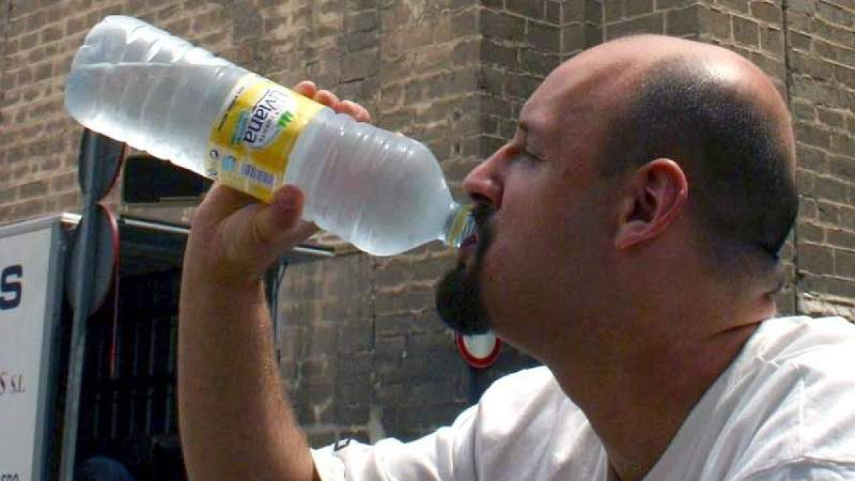 Un hombre bebe de una botella de agua mineral.