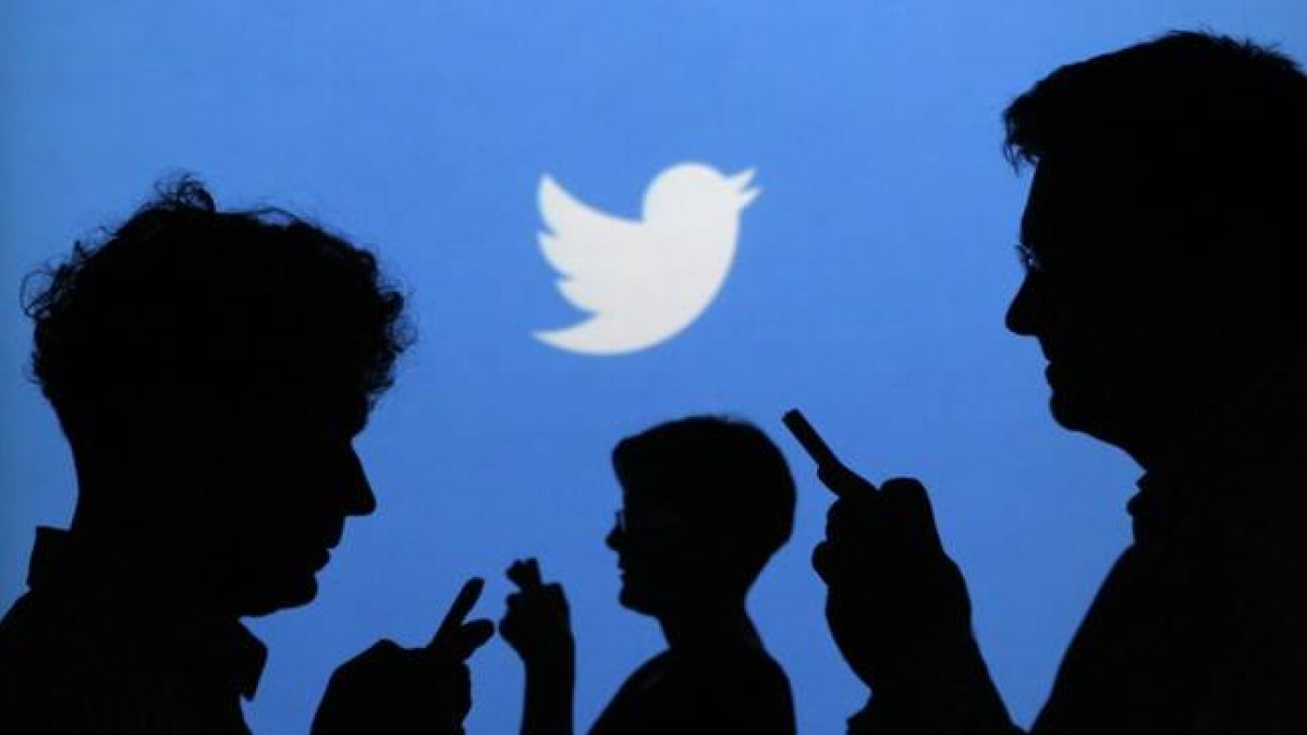 Siluetas de gente con el móvil, con el logo de Twitter al fondo.