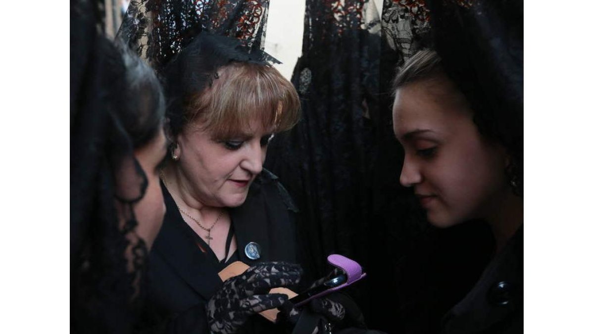 Ansiosas por el comienzo inminente de la procesión, un grupo de manolas consultan sus teléfonos. Estampa de pasado y de futuro.