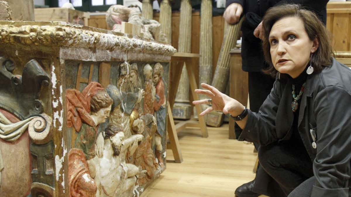 La restauradora Marta Eva Castellanos agachada ante el retablo de Grajalejo de las Matas, devorado por las termitas, como se ve en la foto de la derecha.