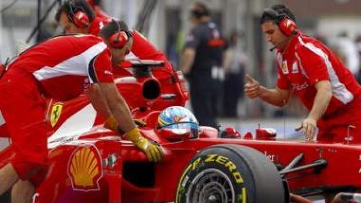 Fernando Alonso conduce su monoplaza, ayudado por los mecánicos, rumbo a boxes.