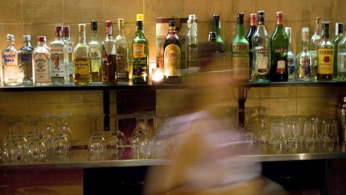 Una mujer, delante de la barra de un bar llena de bebidas