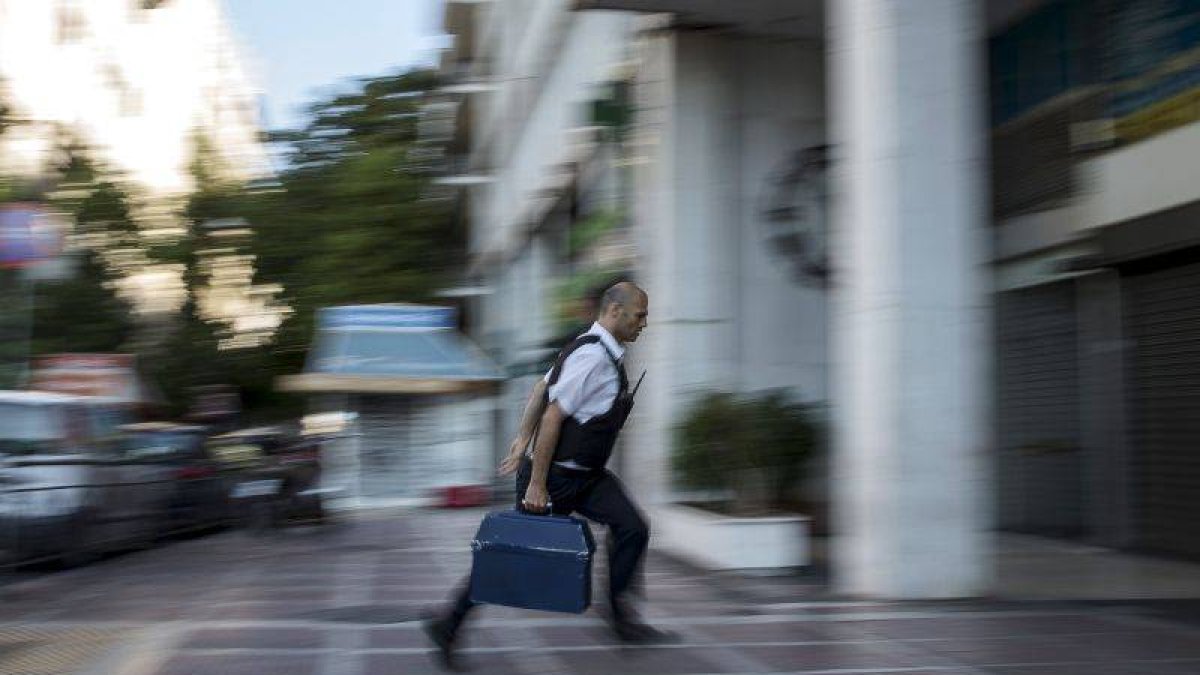 Un hombre entra dinero con una maleta en una sucursal bancaria de Atenas.