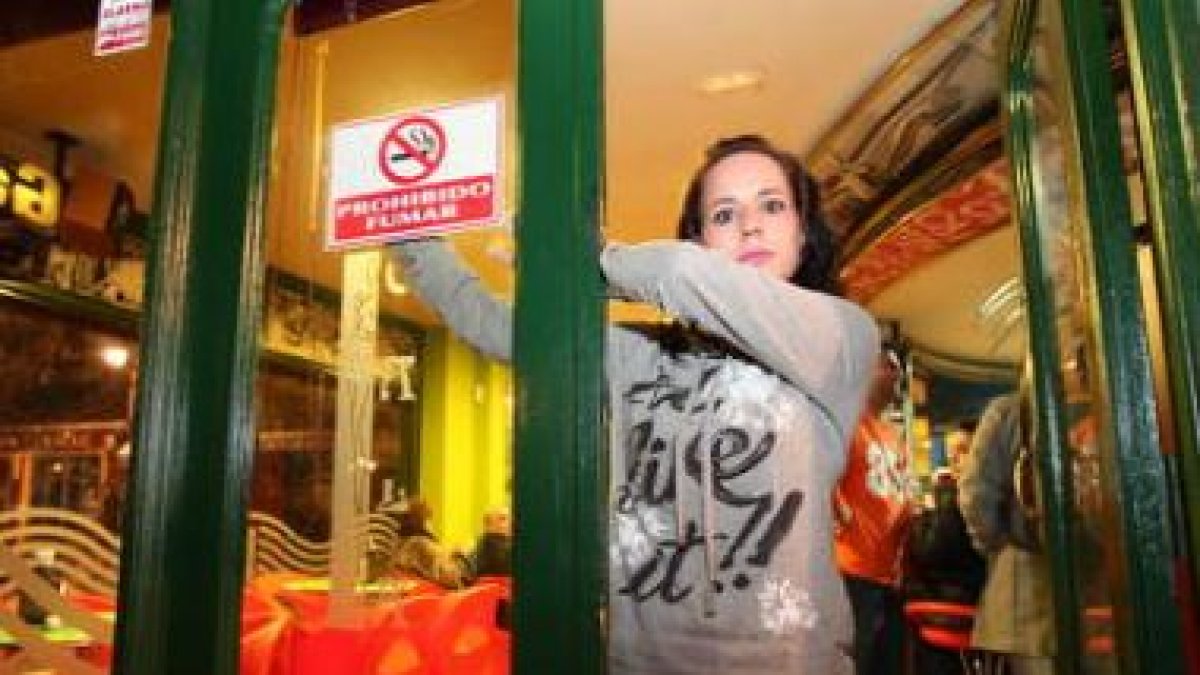 Una trabajadora coloca el cartel de prohibido fumar por la Ley Antitabaco.
