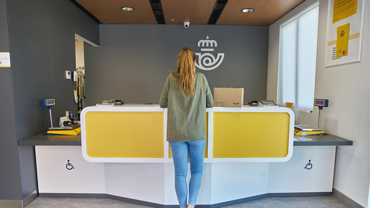 Una mujer realiza trámitres en una oficina de Correos.
