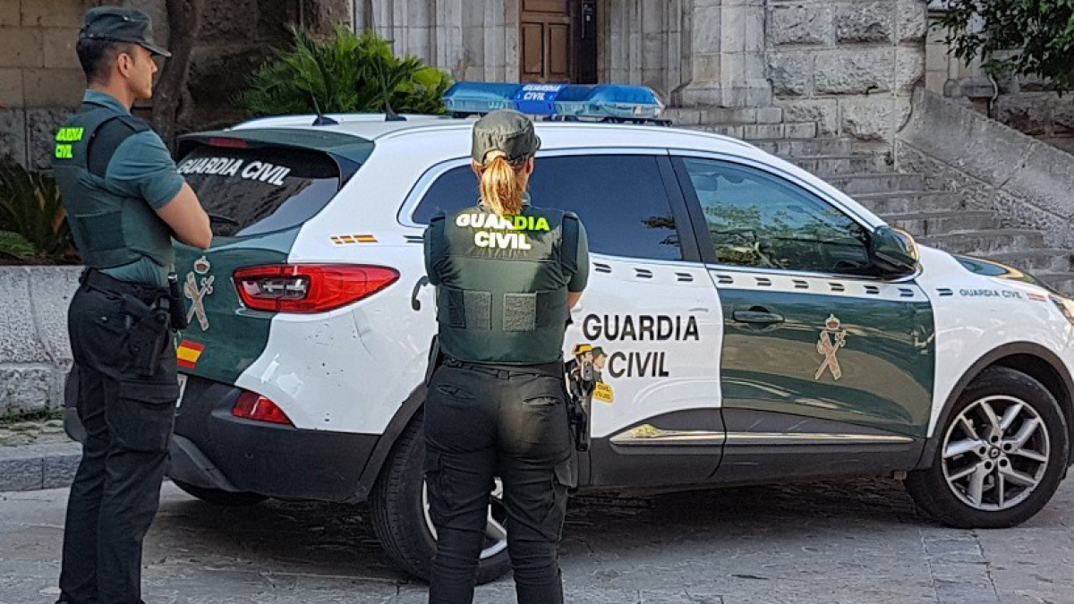 Archivo - Dos agentes de la Guardia Civil junto a un coche oficial.