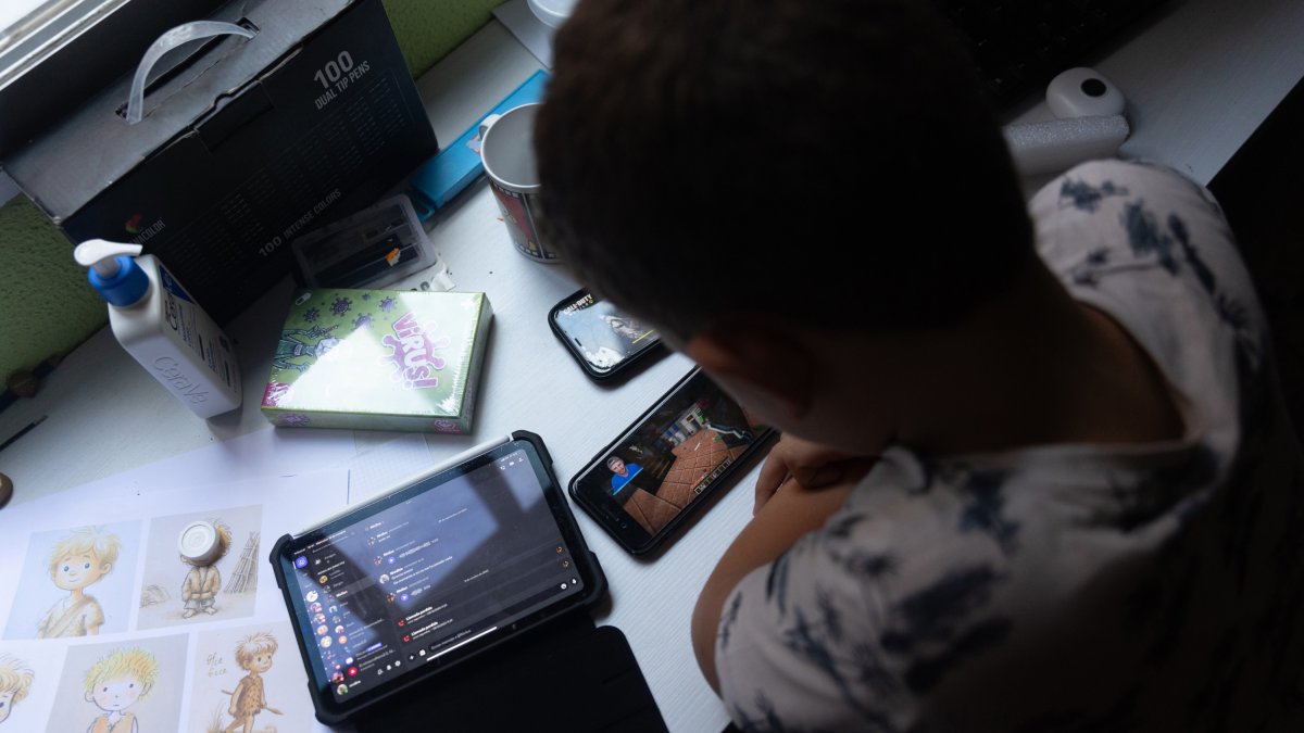 Archivo - Un niño usa el teléfono móvil y una tablet.