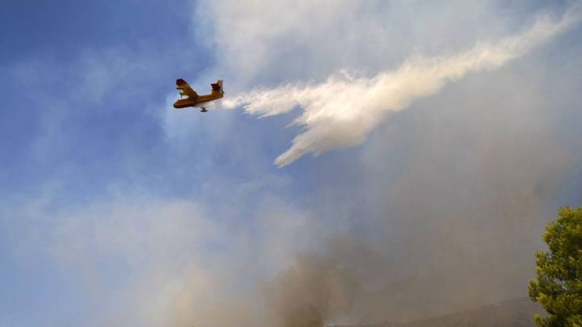 Un avión lanza agua sobre el incendio forestal.