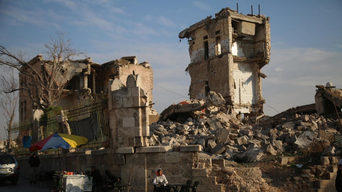 Un vendedor ambulante se sienta el 5 de diciembre de 2024 frente a un edificio dañado mientras la gente se reúne en el lado de la Ciudadela de Alepo (Siria). EFE/EPA/BILAL AL HAMMOUD