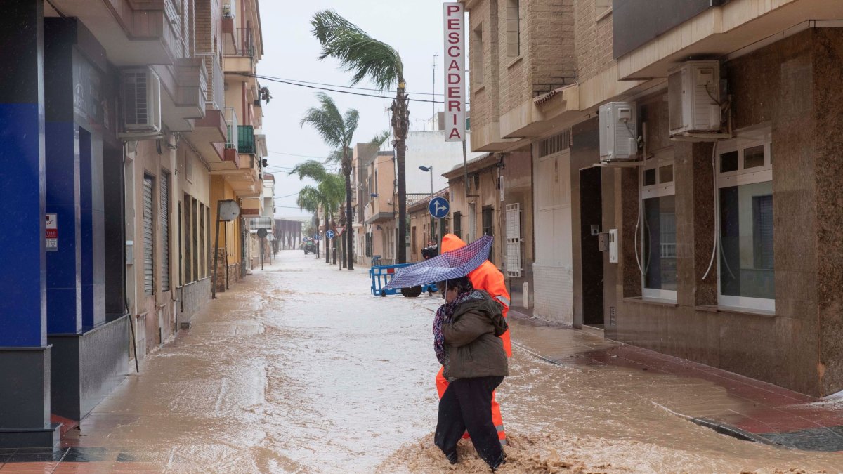 Un voluntario de protección civil ayuda a una mujer a cruzar una calle inundada a causa de las fuertes lluvias caídas.