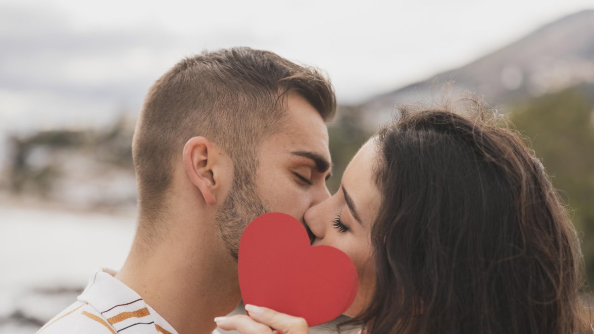 Dos enamorados se besan tras el símbolo de un corazón.